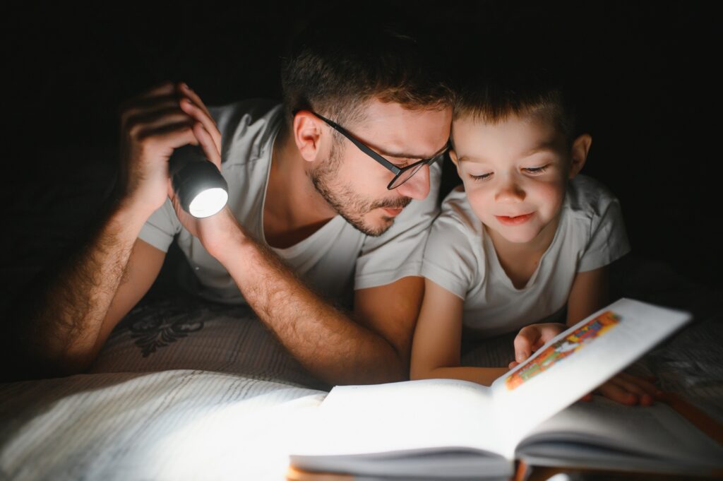 Happy family reading bedtime story under blanket in evening